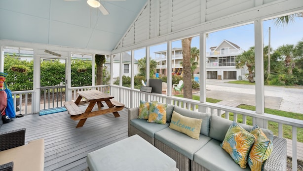 Un espace extérieur abrité doté d’une terrasse en bois, d’un canapé avec des coussins, d’une table et d’un ventilateur de plafond.