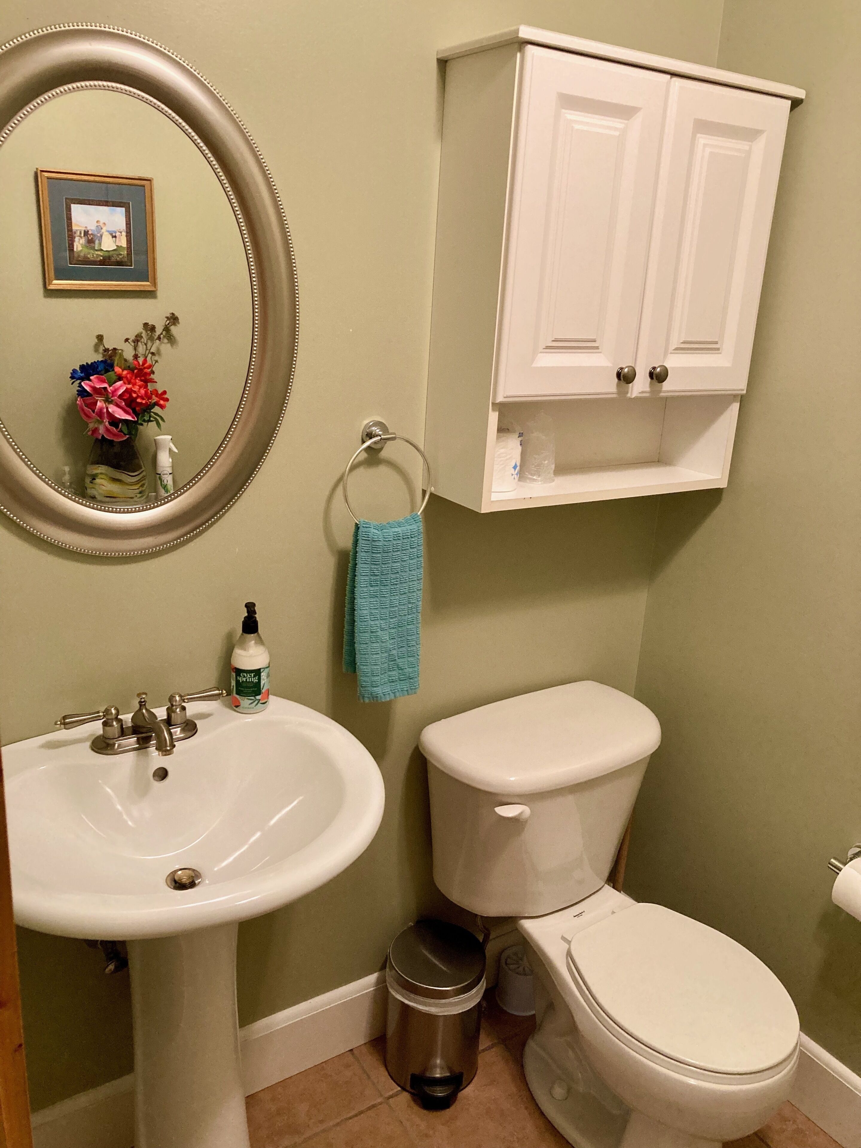 Une salle de bain avec un lavabo blanc, des toilettes, une poubelle, un porte-serviettes et un meuble au-dessus des toilettes.