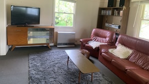 A living room with a TV, a wooden cabinet, a red leather sofa, a small wooden table, and a bookshelf. - Perfect as a Falls Creek base camp. Pet friendly.  (Mount Beauty)