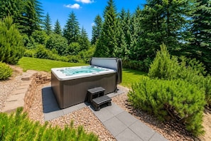 Un bain à remous dans un jardin, avec un chemin de pierres, entouré de verdure et d’arbres.