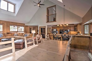 A spacious living area with a large wooden dining table, a sofa set, and a kitchen with wooden cabinets and a central island.