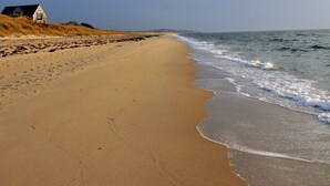 Ampia spiaggia sabbiosa con onde calme, un edificio bianco a sinistra e cielo sereno.