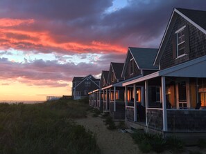 A row of beach houses with a sandy path leading to them, under a sunset sky. - Cottage #11 - Spectacular views of Cape Cod Bay on a private association beach! (Truro)