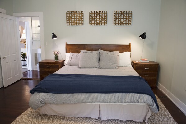 A bedroom with a wooden headboard, a bed with striped bedding, two bedside tables with lamps, and decorative wall art.