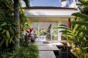 Een modern huis met een glazen deur die uitkomt op een patio, omringd door weelderige tropische planten.
