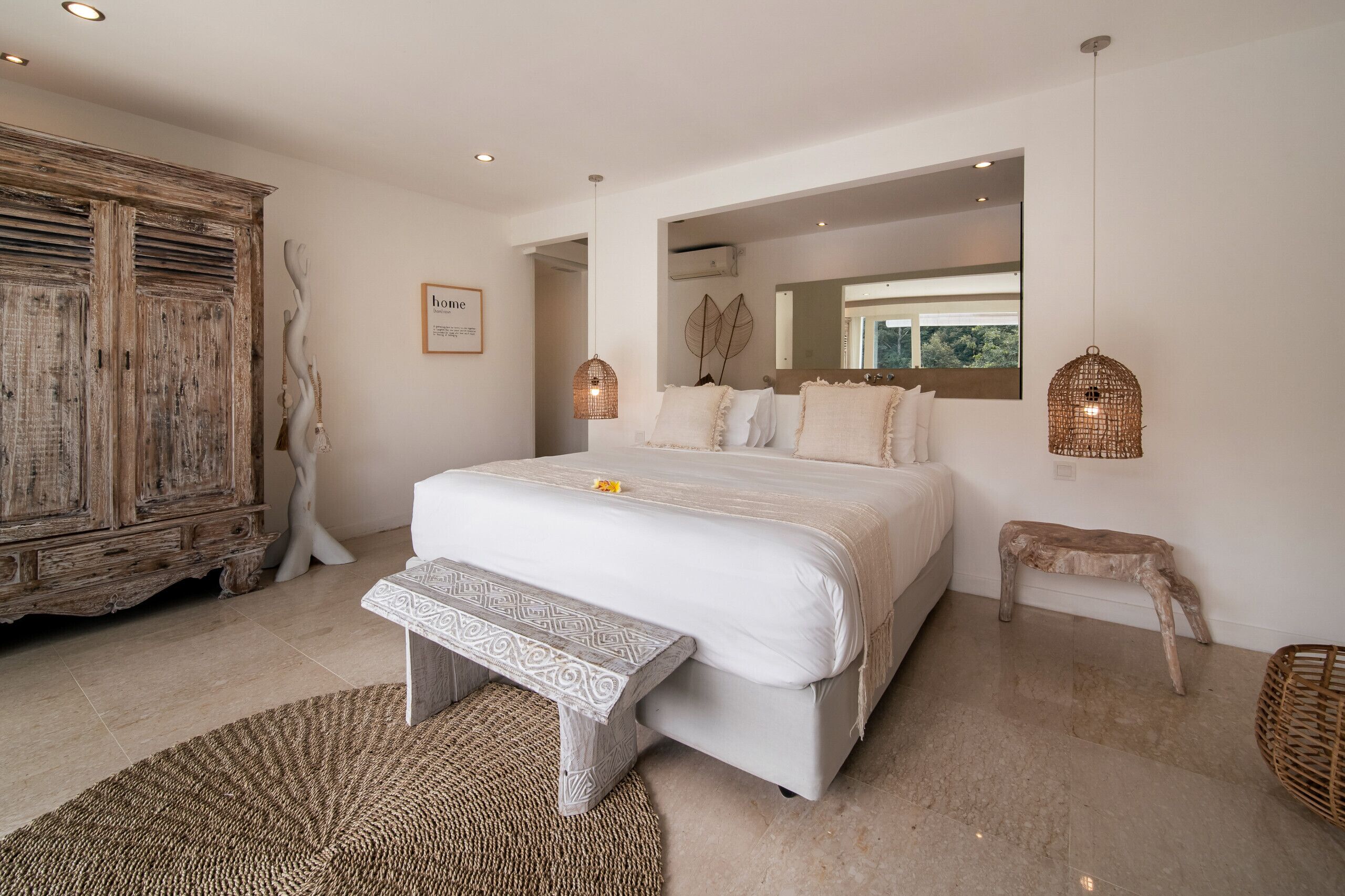 A bedroom with a large bed, a wooden cabinet, a bench, and two wall-mounted lights.
