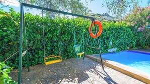 A poolside area with a swing set, a small pool, and a stone pathway. - Casa Rural la Sacri Guaro by Ruralidays (Málaga)