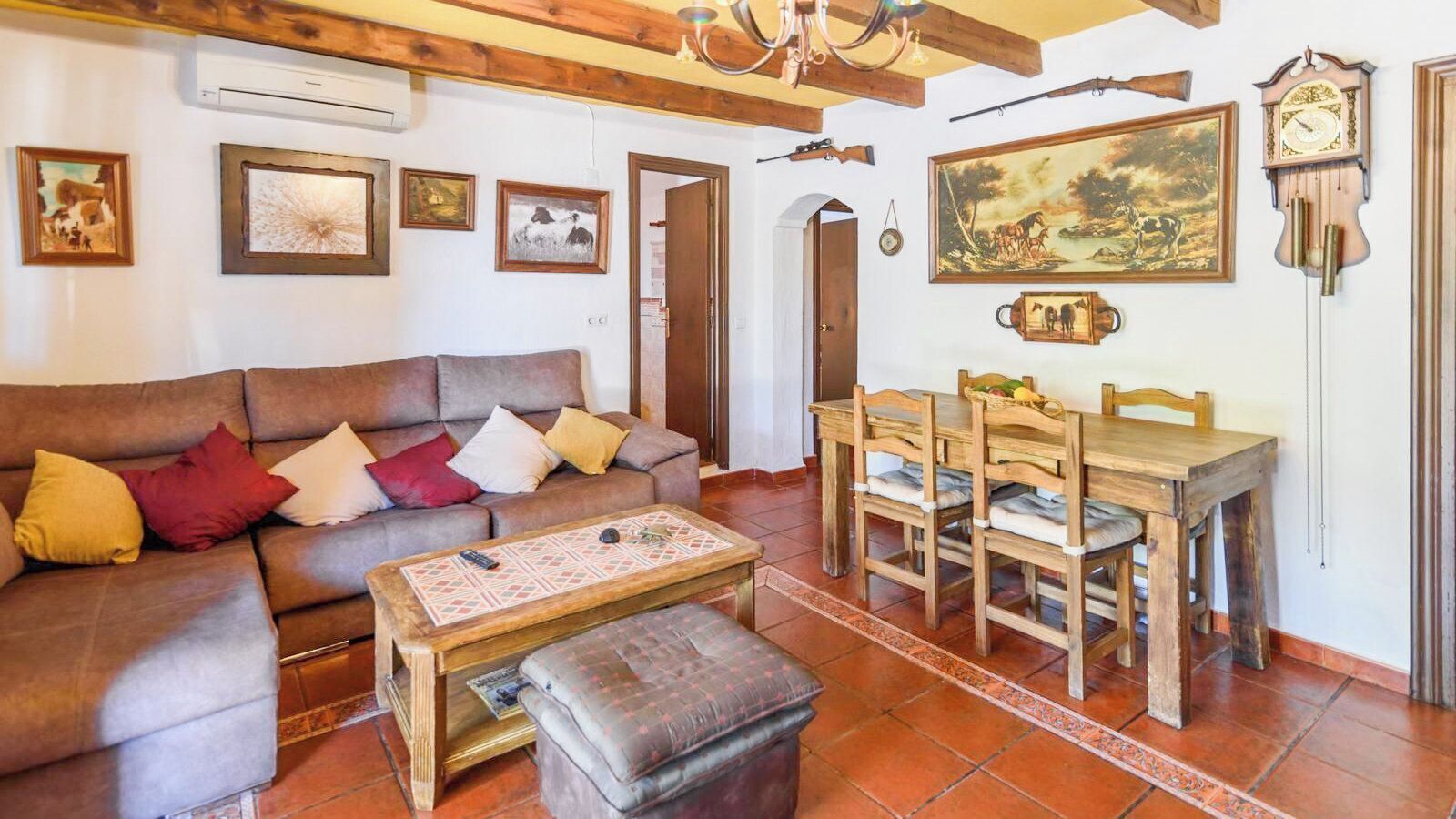 Una sala de estar con un sofá, una mesa de centro y una mesa de comedor con sillas. Hay relojes de pared y cuadros enmarcados.