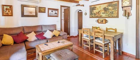 Una sala de estar con un sofá, una mesa de centro y una mesa de comedor con sillas. Hay relojes de pared y cuadros enmarcados.