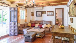 A cozy living room with a sofa, ottoman, and a wooden dining table with a fruit basket. - Casa Rural la Sacri Guaro by Ruralidays (Málaga)
