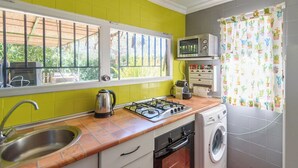 A compact kitchen with a gas stove, a microwave, a sink, and a washing machine. - Casa Rural la Sacri Guaro by Ruralidays (Málaga)
