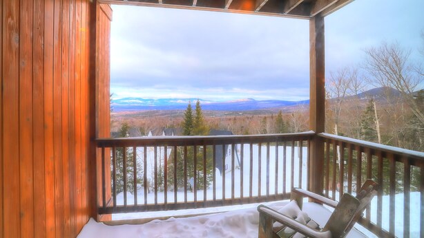 Eine Holzhütte mit Balkon und Blick auf eine verschneite Landschaft sowie ferne Berge.