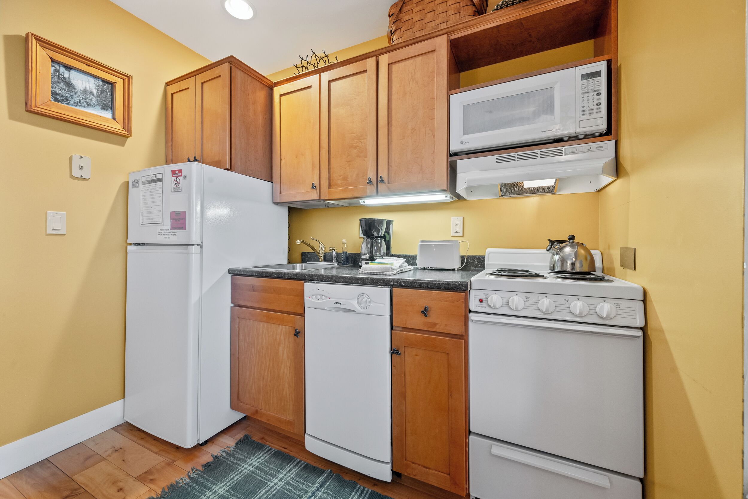 A kitchen with wooden cabinets, a white refrigerator, a dishwasher, a microwave, and a stove.