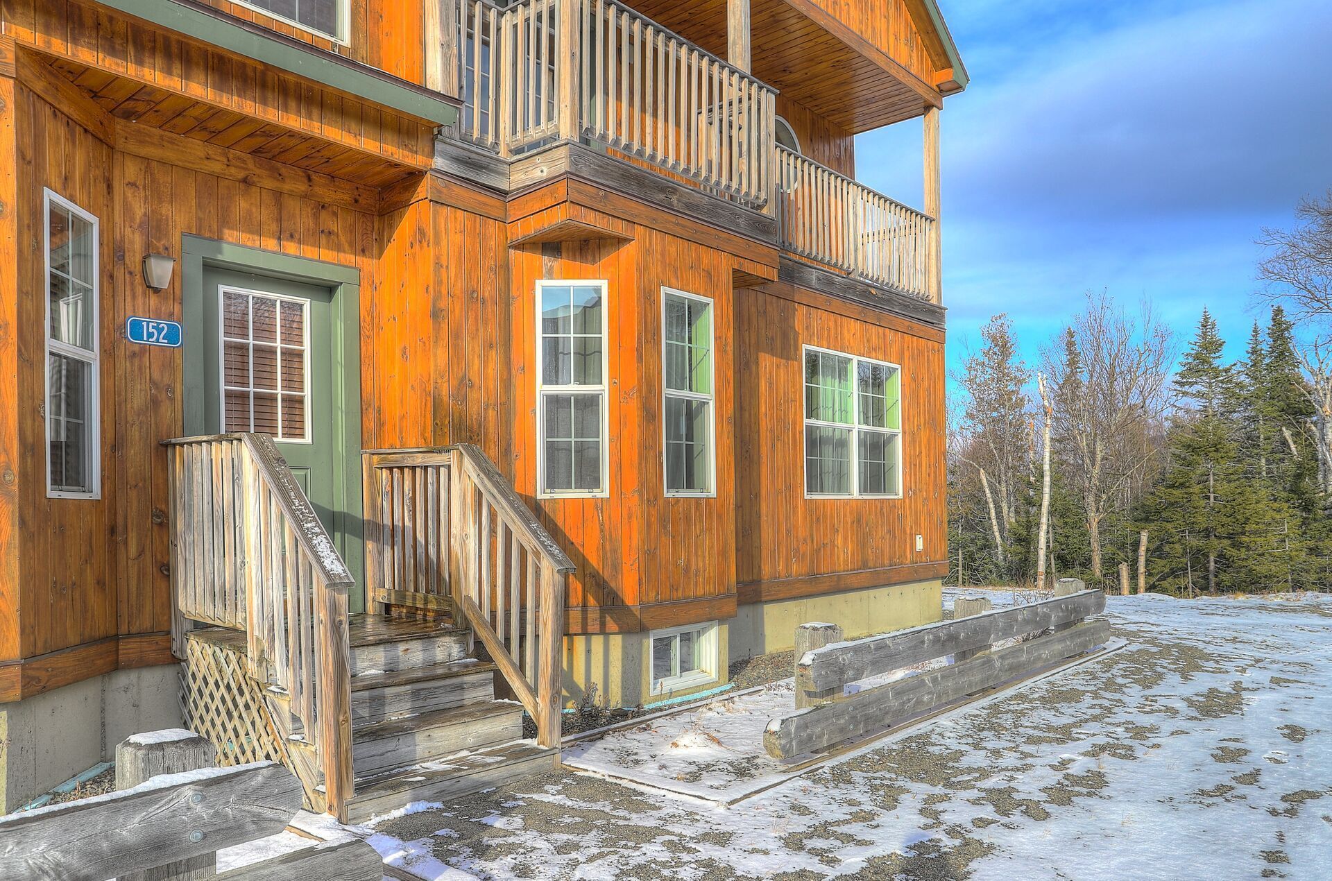 A wooden cabin with a green door, multiple windows, and a balcony.