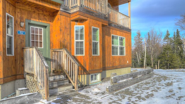A wooden cabin with a green door, multiple windows, and a balcony.