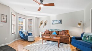 A living room with a ceiling fan, a brown sofa, a blue armchair, a coffee table, and a rug.