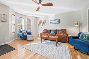 A living room with a ceiling fan, a brown sofa, a blue armchair, a coffee table, and a rug. - Mountain Brook 152 - Ski in Ski out at Saddleback (Sandy River Plantation)