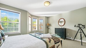 A bedroom with a bed, dresser, mirror, lamp, and a telescope.