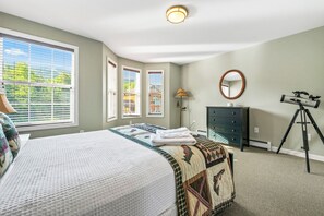 A bedroom with a bed, dresser, mirror, lamp, and a telescope. - Mountain Brook 152 - Ski in Ski out at Saddleback (Sandy River Plantation)