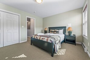 A bedroom with a bed, nightstands, a lamp, and a door. - Mountain Brook 152 - Ski in Ski out at Saddleback (Sandy River Plantation)