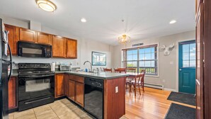A modern kitchen with wooden cabinets, a built-in oven, microwave, and dishwasher, a large island with seating, and a view of the outdoors through a window.