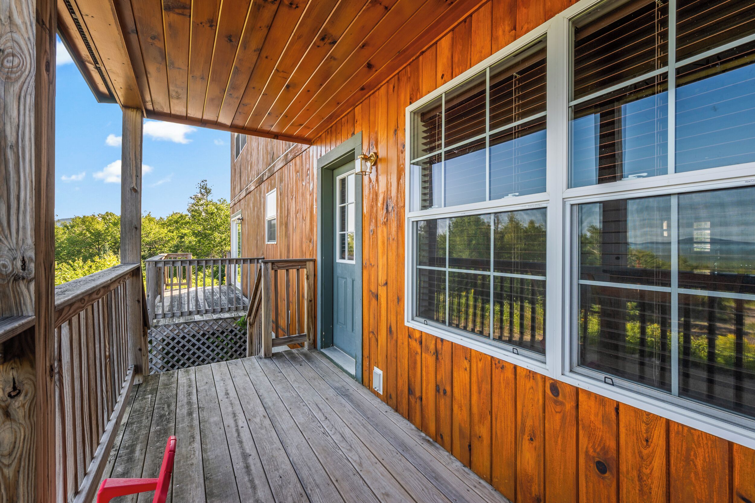 A wooden deck with a railing, a door, and large windows.