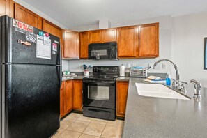 A kitchen with wooden cabinets, a black refrigerator, a microwave, a stove, and a sink. - Mountain Brook 152 - Ski in Ski out at Saddleback (Sandy River Plantation)