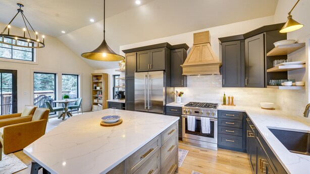 Una cocina moderna con una isla grande, muebles oscuros, electrodomésticos de acero inoxidable e iluminación colgante.