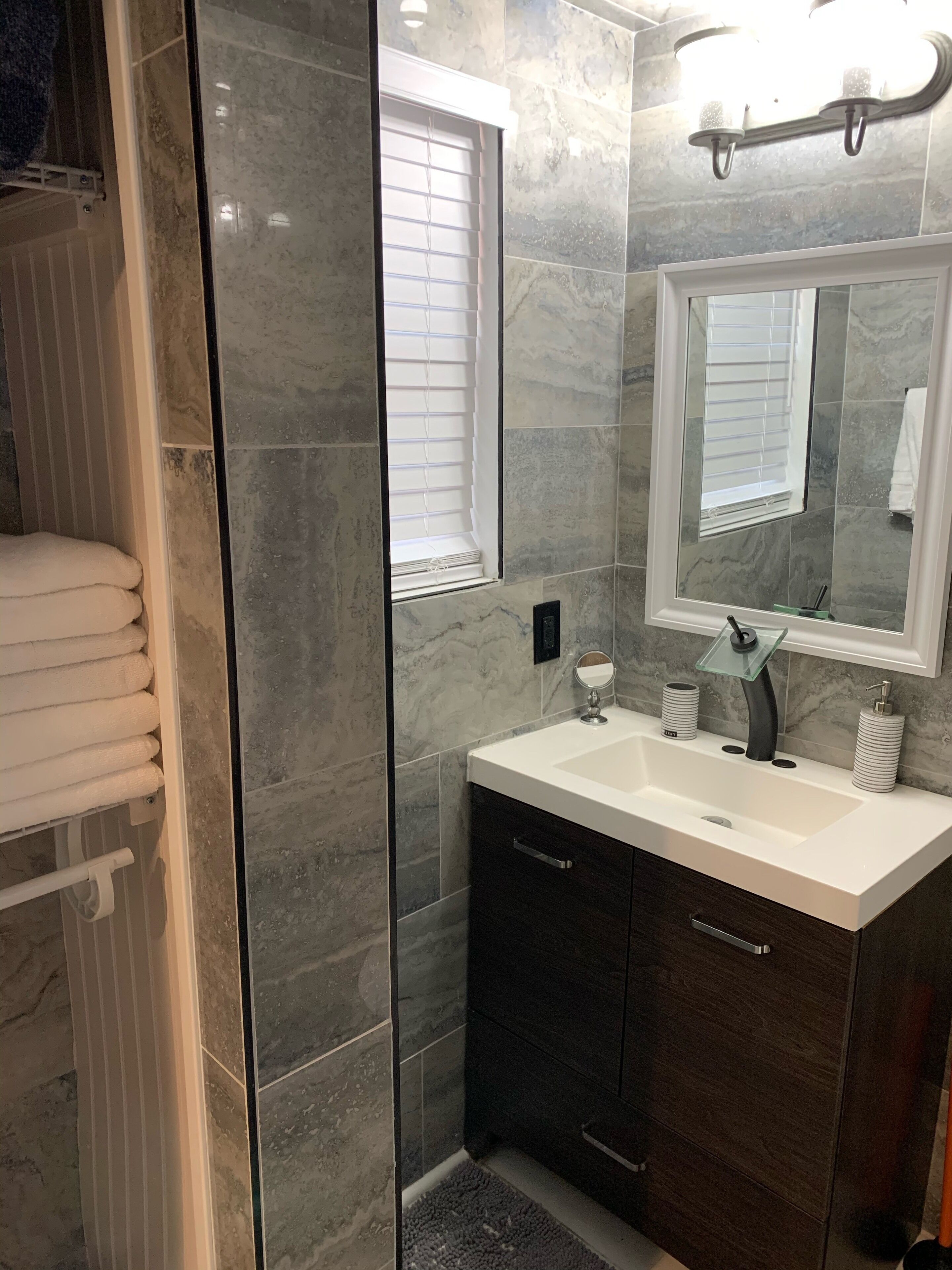 Un bagno moderno con box doccia in vetro, un lavabo bianco con mobile contenitore scuro e un grande specchio sopra il lavabo.
