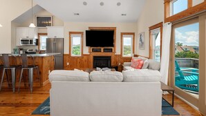 Eine moderne Küche mit einer großen Kochinsel, ein Essbereich mit einem weißen Sofa und ein Wohnzimmer mit Kamin.