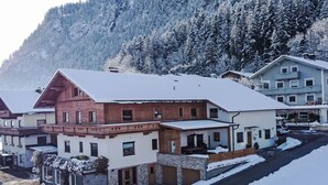 A snow-covered building with a wooden facade and a stone base, surrounded by snow-covered trees and a mountain in the background. - Nice apartment for 8 guests with WIFI, TV, patio and pets allowed (Strass Im Zillertal)