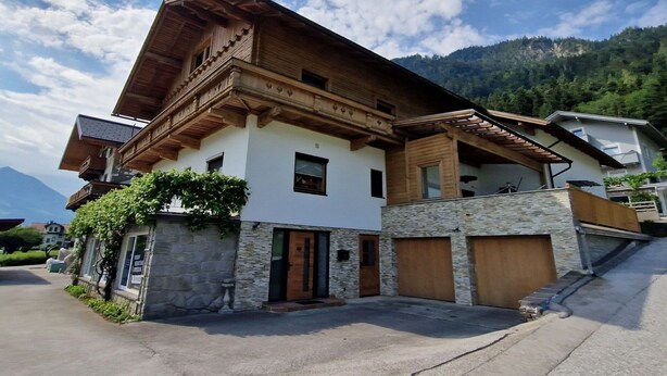 A two-story house with a stone facade, wooden balcony, and a garage. - Nice apartment for 8 guests with WIFI, TV, patio and pets allowed (Strass Im Zillertal)