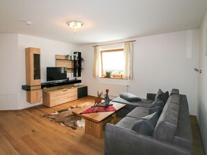 Una sala de estar con una mesa de centro de madera, sofá gris, televisor, estanterías de madera y una ventana con cortinas.
