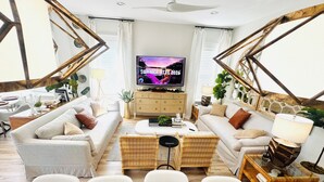 A living room with a sofa, chairs, a coffee table, a TV, and a decorative wall. -  SANDSCASTLE :Luxury: Iconic Retreat,Sleeps 16, Heated Pool, Beach Steps Away  (Panama City Beach)
