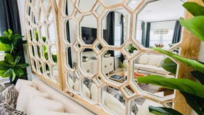 A living room with a white sofa, a decorative wooden partition, and a large mirror reflecting the room. -  SANDSCASTLE :Luxury: Iconic Retreat,Sleeps 16, Heated Pool, Beach Steps Away  (Panama City Beach)