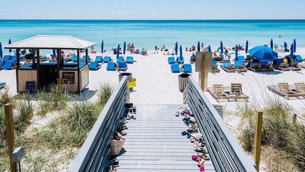 A beach with a wooden walkway leading to a beach hut, blue lounge chairs, and umbrellas. -  SANDSCASTLE :Luxury: Iconic Retreat,Sleeps 16, Heated Pool, Beach Steps Away  (Panama City Beach)