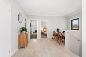 Enter a serene space with a hallway leading to a bedroom and dining area, featuring a cabinet, wall clock, and door to the bedroom.