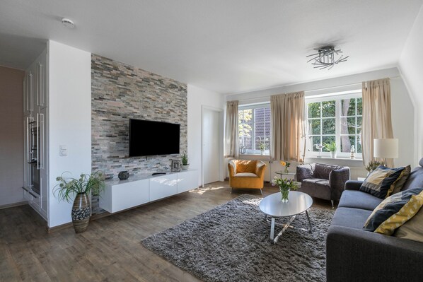 A modern living room with a flat-screen TV, a stone wall, a sofa, a coffee table, and a window with curtains.
