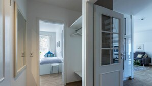 A modern interior with a hallway leading to a bedroom, a closet with hanging space, and a seating area with a sofa and cushions. - Bright & Charming Vacation Apartment "Kille - Right Apartment" in Sankt Peter Ording (St. Peter-Ording)