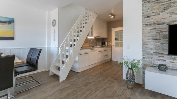 A modern kitchen with white cabinets, a wooden staircase, and a stone accent wall. - Bright & Charming Vacation Apartment "Kille - Right Apartment" in Sankt Peter Ording (St. Peter-Ording)