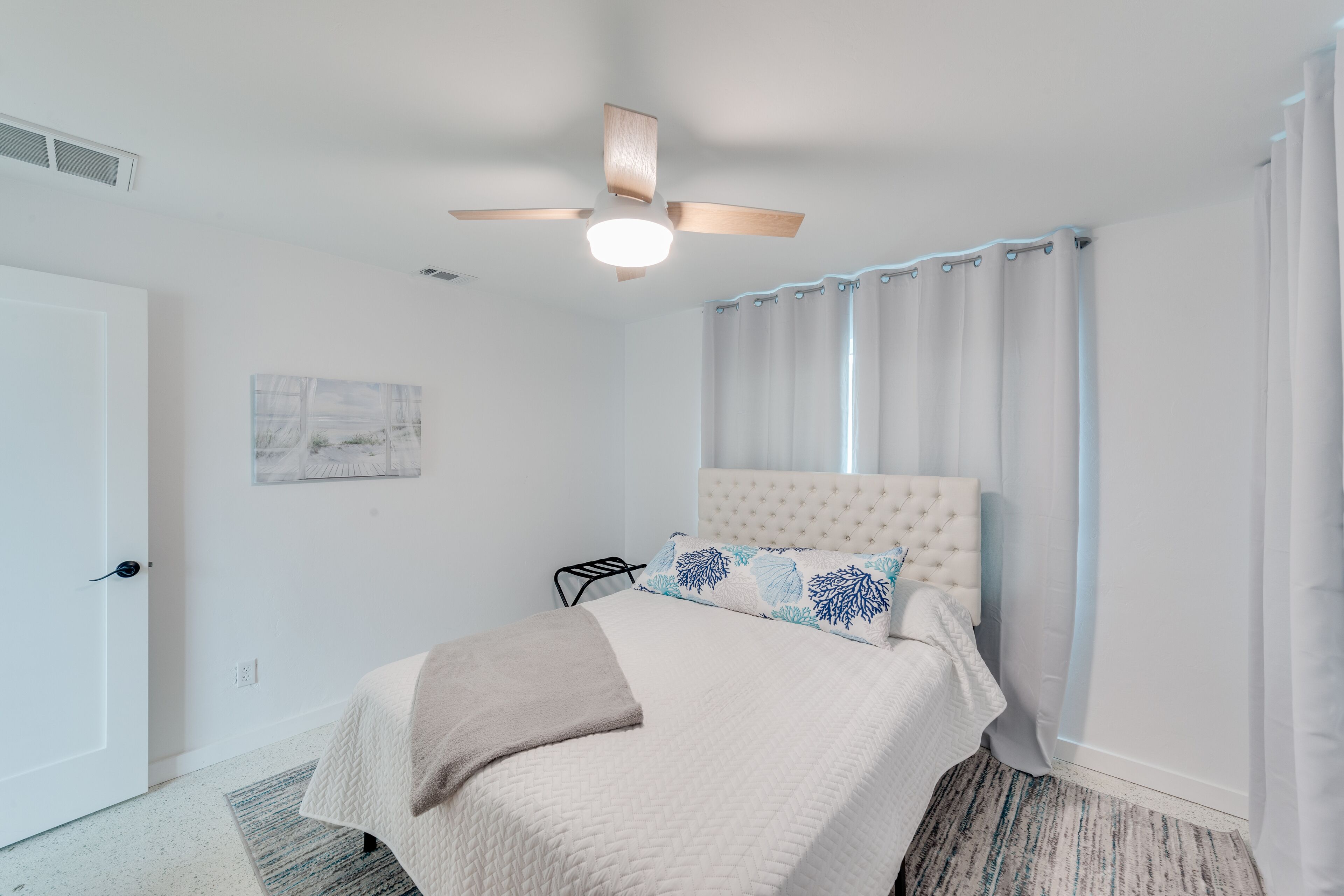 Une chambre à coucher avec un lit, un ventilateur de plafond, une porte et une fenêtre avec des rideaux.