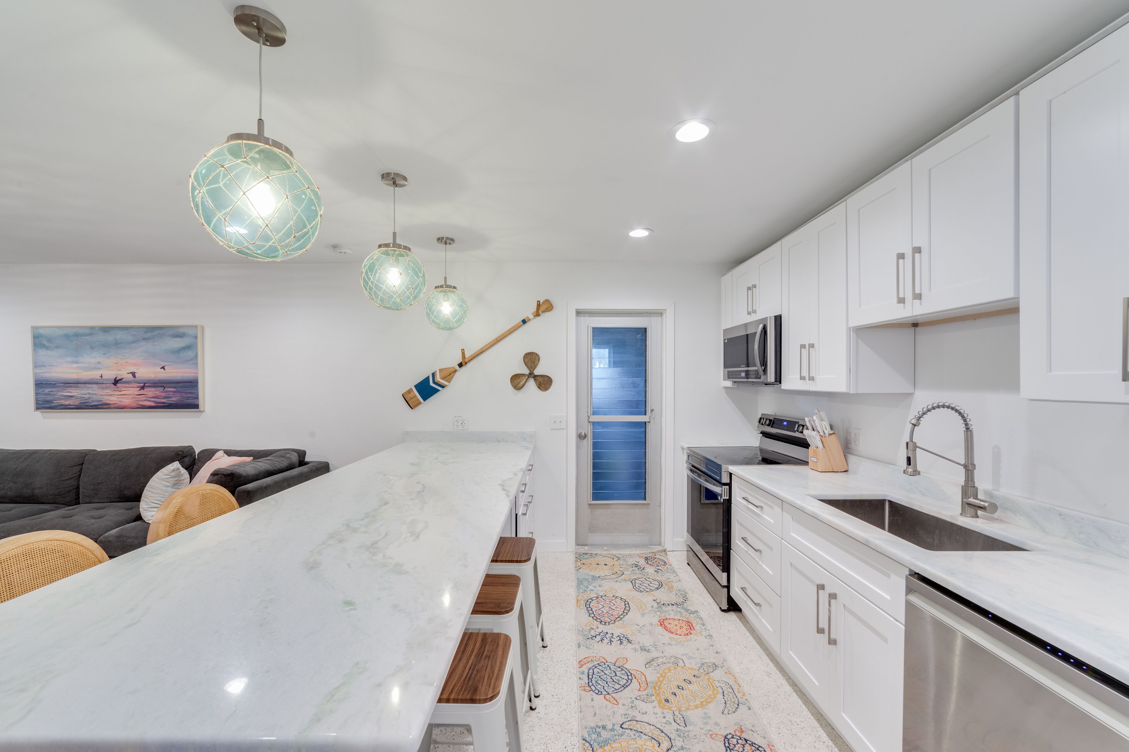A modern kitchen with white cabinets, a marble countertop, and pendant lights.