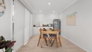 Een moderne keuken met witte kasten, een koelkast en een eethoek met een houten tafel en stoelen.