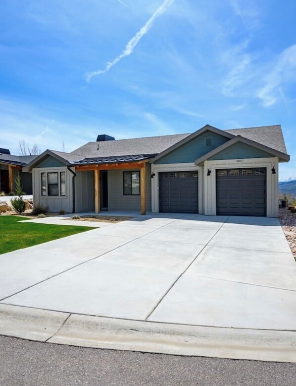 A modern two-story house with a covered patio, a garage, and a well-maintained lawn.