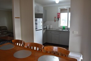 Une cuisine compacte équipée d’un réfrigérateur, d’un évier et d’une fenêtre. On aperçoit une table à manger avec des chaises au premier plan.