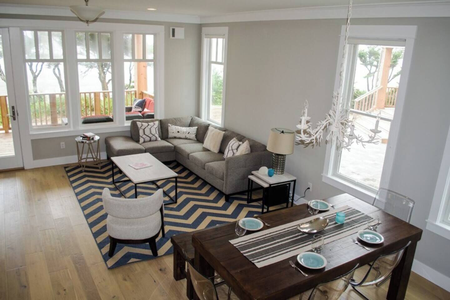 A spacious living room with a sectional sofa, a dining table set for four, and a large window providing natural light.