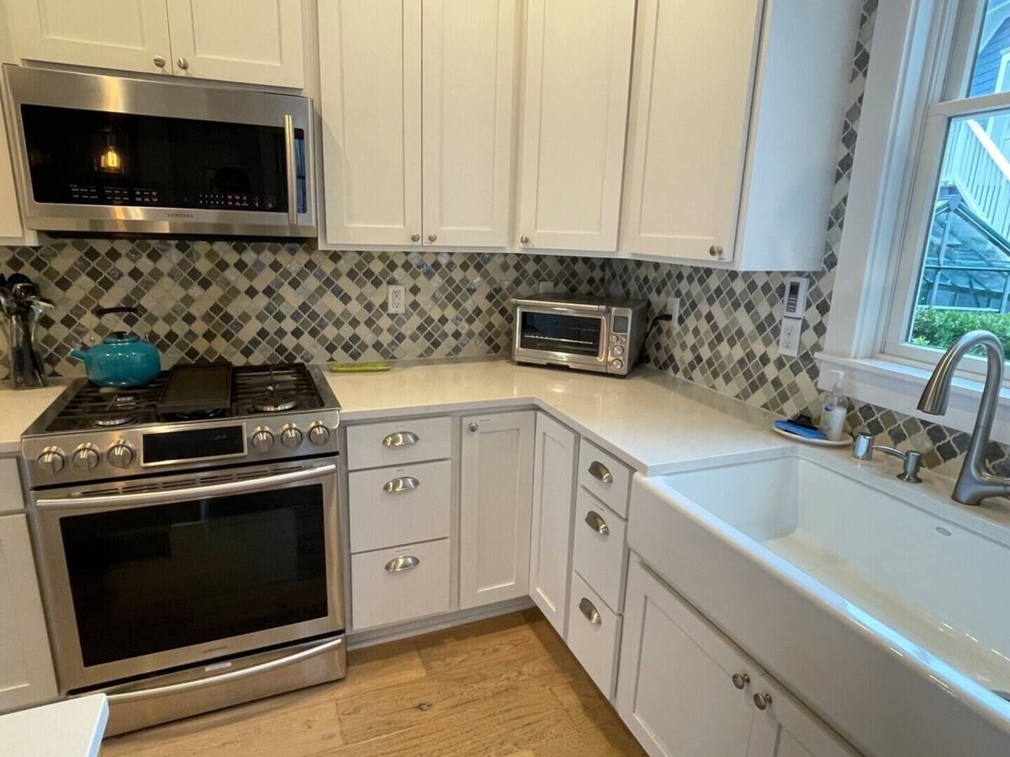 A modern kitchen with white cabinets, stainless steel appliances, a microwave, a toaster, and a sink.