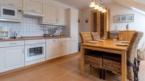 A modern kitchen with white cabinetry, a wooden dining table, wicker chairs, and a hanging light fixture. - Ferienwohnung 7 "auszeit" in der Villa Annabelle (Binz)