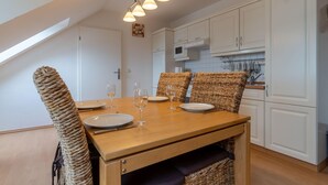A dining area with a wooden table set for four, surrounded by wicker chairs, white cabinets, and a kitchen in the background. - Ferienwohnung 7 "auszeit" in der Villa Annabelle (Binz)