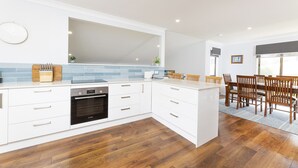 A modern kitchen with white cabinetry, a Bosch oven, a blue-tiled backsplash, and a dining area with wooden chairs and a table.